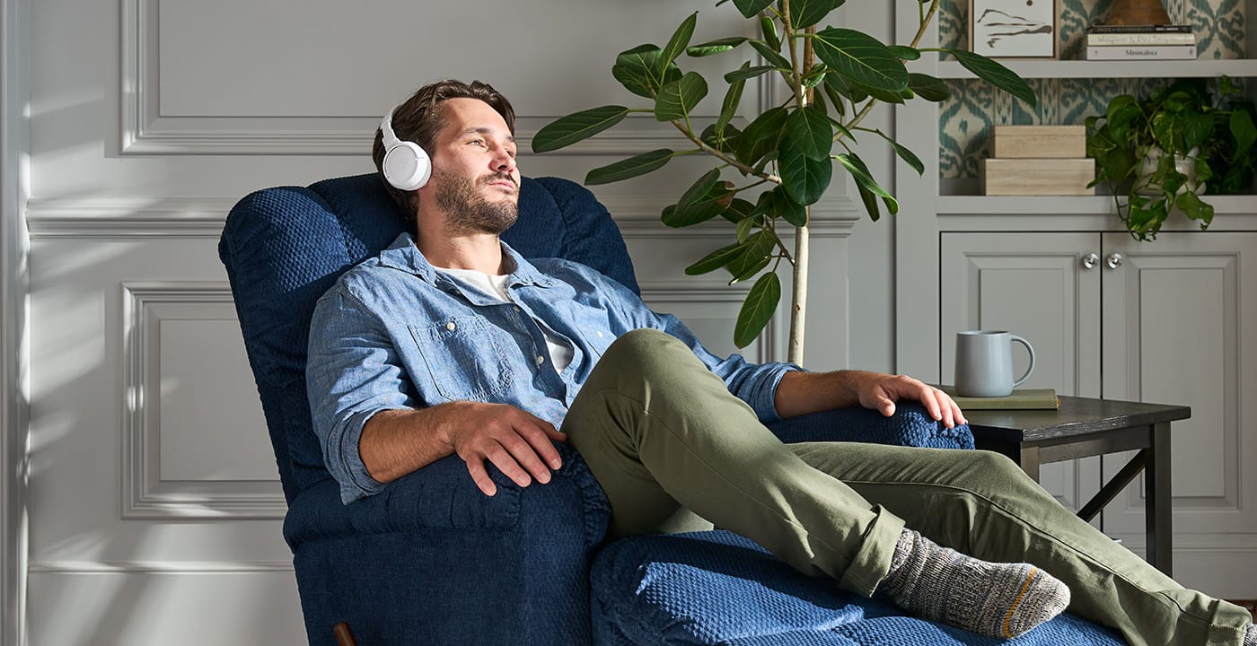 A man relaxing in a navy La-Z-Boy recliner with headphones on, beside a houseplant